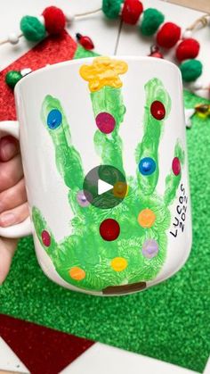 a person holding a coffee mug with a handprinted green christmas tree on it