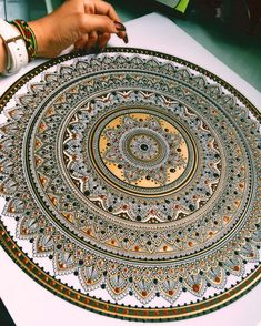 a person is working on an intricately designed round rug with gold and white colors