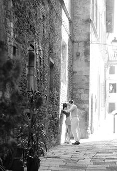 black and white photograph of two people kissing in an alleyway between buildings on either side