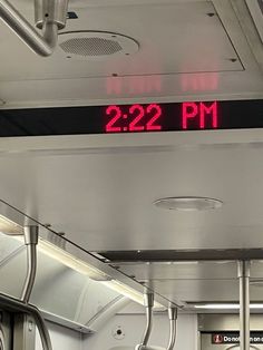 a red clock that reads 22 22 pm is on the ceiling of a subway car