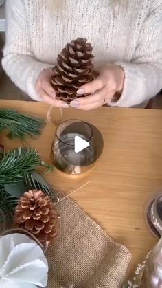 a person holding a pine cone on top of a wooden table next to christmas decorations