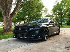 a black car parked in front of a tree on the side of a road next to a sidewalk