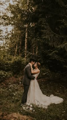 a bride and groom are kissing in the woods on their wedding day, surrounded by tall trees