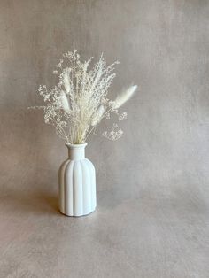 a white vase filled with flowers on top of a table next to a gray wall