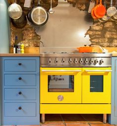 a yellow stove top oven sitting inside of a kitchen next to blue drawers and cabinets