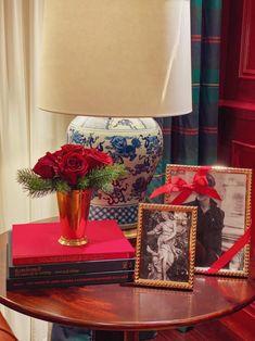 a table topped with books and a vase filled with red roses next to a lamp