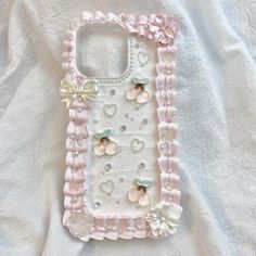 a cell phone case made out of pink and white material with pearls, bows and jewels on it