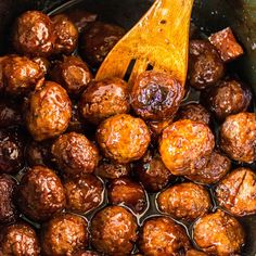 the meatballs are being cooked in the slow cooker with a wooden spatula