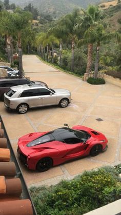 two red sports cars are parked in front of a house with palm trees and mountains behind them