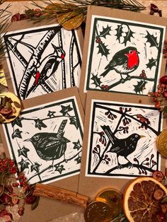 four cards with birds on them sitting next to oranges and pine cones, surrounded by christmas decorations