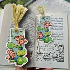 an open book with flowers and leaves on the pages is being held in someone's hand