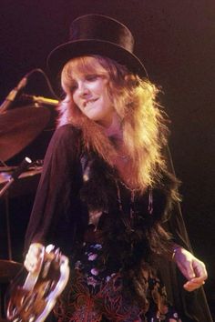 a woman wearing a black hat and dress with fur on her shoulders, standing in front of a microphone