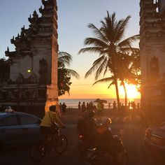 two people riding bikes on the beach at sunset with palm trees in the foreground