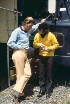 two people standing next to each other in front of a blue and yellow truck with the door open