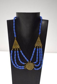 This is a Old 1960 African Turkana Brass Round and Triangle Multi Strand Beaded Necklace with Blue Glass from Kenya. The necklace is strung on wire with a a brass hook and eye clasp.  A wonderful gift for a woman or man. Necklace 20" Long 30mm Round Brass Pendant 36mm Long Triangle Beads 6mm Round Blue Beads AT BACARA WE STAND BEHIND ALL OF OUR MERCHANDISE. WE CAN PROVIDE REFERENCES FOR ALL ARTIFACTS THAT WE SELL, AS WELL AS DOCUMENTATION TOWARD THEIR AUTHENTICITY. FULL MONEY BACK GUARANTEE WILL BE PROVIDED FOR DISSATISFIED CUSTOMERS. YOUR SATISFACTION IS OUR MAIN GOAL, AND WE THANK YOU FOR SHOPPING AT THE WORLD OF BACARA. G323 #22 Adjustable Brass Necklace With Large Beads, Blue Beaded Brass Necklaces, Blue Metal Amulet Jewelry, Blue Brass Jewelry For Jewelry Making, Artisan Blue Metal Necklace, Adjustable Bronze Necklace With Polished Beads, Unique Blue Brass Jewelry, Artisan Blue Nickel-free Necklace, Traditional Blue Brass Jewelry