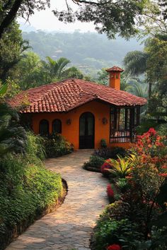 an orange house surrounded by lush green trees and flowers in the foreground is a stone path leading to it