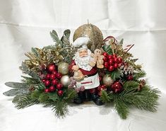 a christmas arrangement with santa clause holding a teddy bear and other holiday decorations on a white background