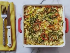 a casserole dish with vegetables in it next to a fork and knife