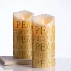 two candles that are sitting next to each other on a white counter top with the words peace written in gold foil