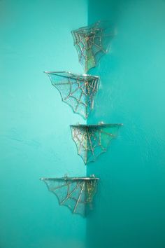 three metal baskets hanging on a wall in the shape of spider webs with water splashing around them