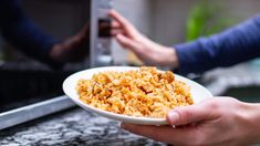 someone is holding a white bowl full of food in front of an oven and microwave