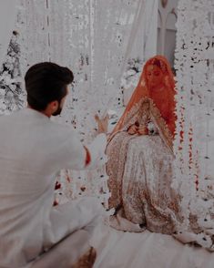 a man kneeling down next to a woman in a white wedding dress and orange veil