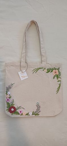 a white bag with flowers on it sitting on top of a bed next to a wall