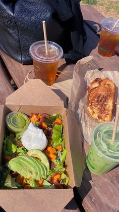 an open box of food sitting on top of a wooden table next to two drinks