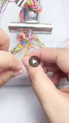 two hands are working on an object with different colored cords and metal spools