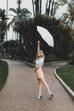 a woman holding an umbrella in the air on a brick walkway with palm trees behind her