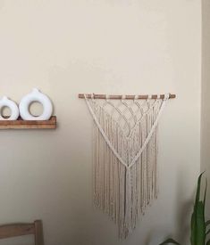 a wall hanging with two white vases on top of it next to a wooden shelf