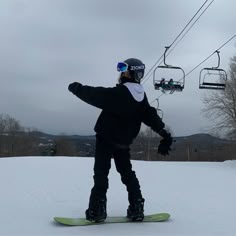 a person riding a snowboard on top of a snow covered slope next to a ski lift