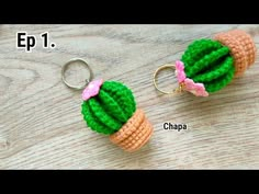 two crocheted cactus keychains with pink bows on them sitting on top of a wooden table