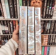 someone holding three books in front of a book shelf