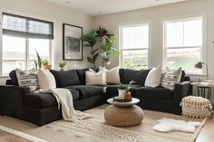 a living room filled with black couches and white pillows on top of a rug