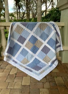 a blue and white quilt hanging on the side of a building with trees in the background