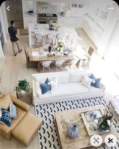 an aerial view of a living room and kitchen area with white couches, blue and white rugs