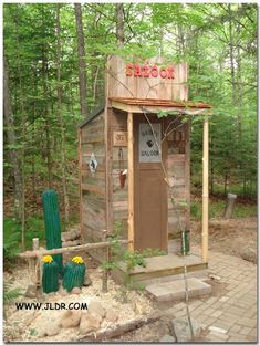 a small outhouse in the woods with cactus growing on it's roof and door