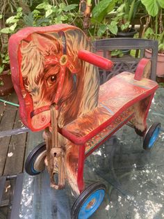 a wooden toy horse pulling a wagon on top of a glass table with plants in the background