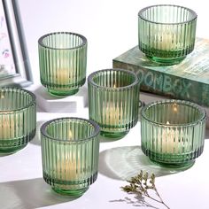 four green glass votives sitting on top of a table next to a book