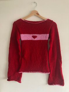 a red sweater with pink and white stripes is hanging on a hanger against a wall