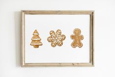 three gingerbread cutouts are displayed in a wooden frame on the wall next to a white wall