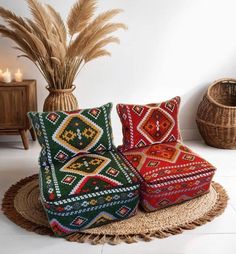 two colorful pillows sitting on top of a rug next to a vase filled with dry grass