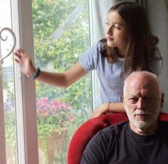 an older man sitting in a red chair next to a woman who is looking out the window