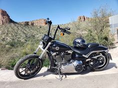 a black motorcycle parked on the side of a road near some bushes and trees with mountains in the background