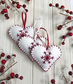 two heart shaped ornaments hanging from red and white ribbons on a wooden table with berries