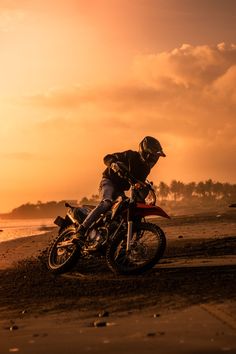 a man riding on the back of a motorcycle down a sandy beach next to the ocean