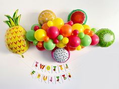 there is a bunch of fruit and balloons on the table with it's name spelled out