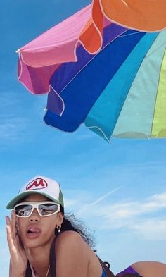 a woman laying on the beach with an umbrella above her head and sunglasses over her face