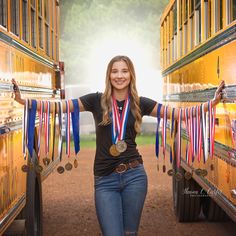 a woman standing in front of two school buses with medals around her neck and arms